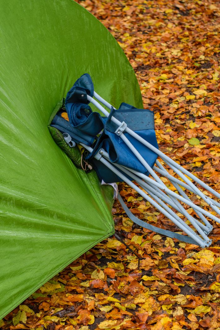 Green tent with a folded camp chair on colorful autumn leaves.