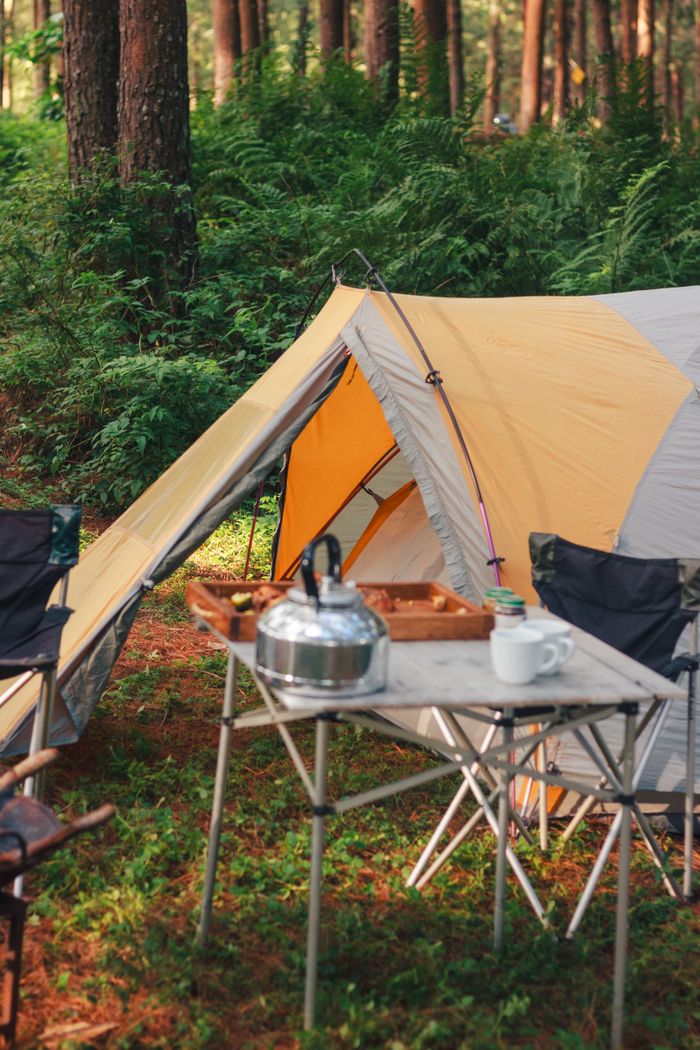 Cozy camping scene with tent, chairs, and table in a lush forest. Ideal for outdoor adventure enthusiasts.