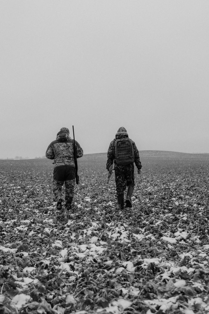 Two armed men in camouflage walking in a snowy field, back view.