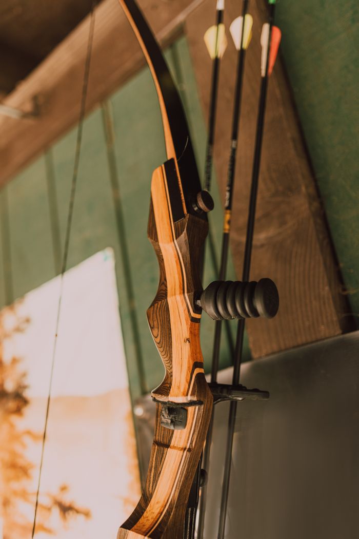 Close-up of a traditional wooden bow with arrows hanging indoors.